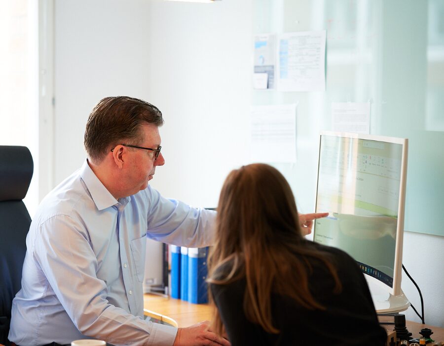 Two colleagues discussing work on a computer screen.