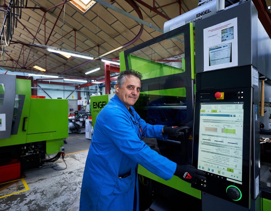 Engineer operating a green injection molding machine in a factory.