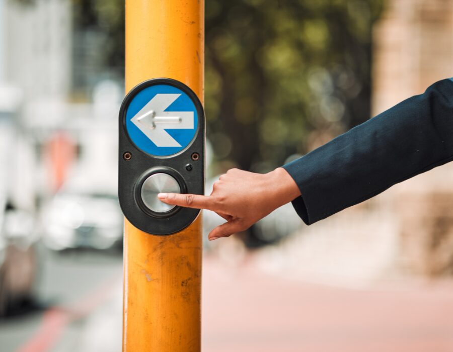 Person pressing a pedestrian crossing button on a pole.