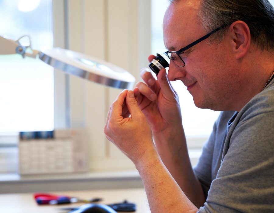 Man inspecting a small object using a magnifying glass.