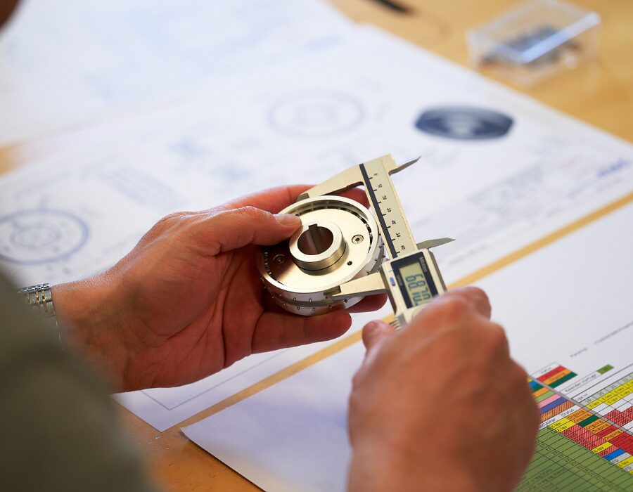 Person measuring a metal component with a caliper.