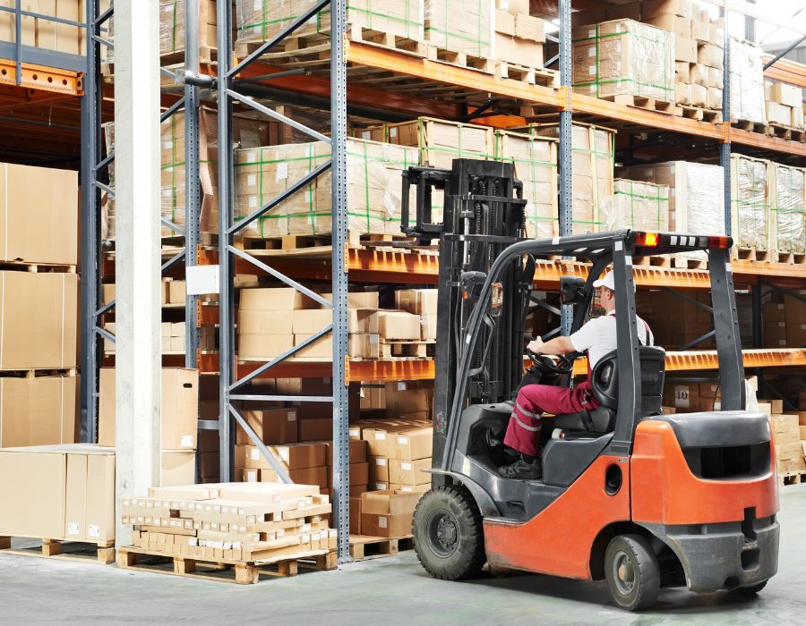 Opérateur conduisant un chariot élévateur orange dans une usine.