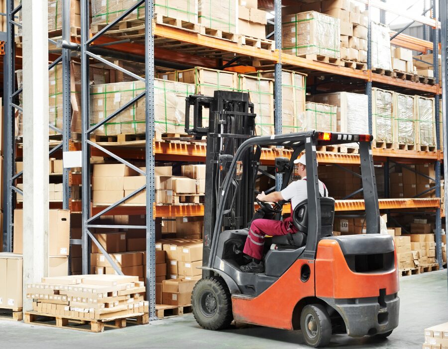 Forklift operator stacking pallets in warehouse.