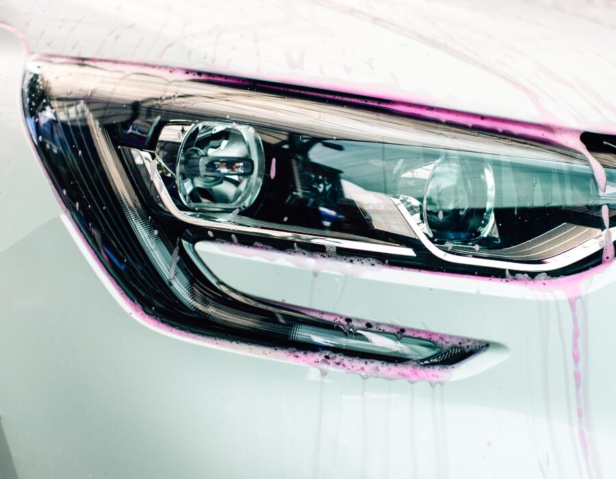 A car headlight covered in soap during a wash.